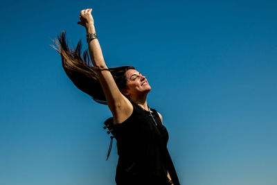 Low angle view of woman jumping against blue sky