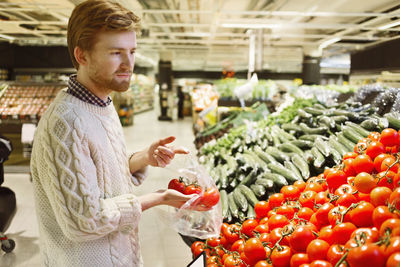 Young man buying fresh tomatoes at supermarket