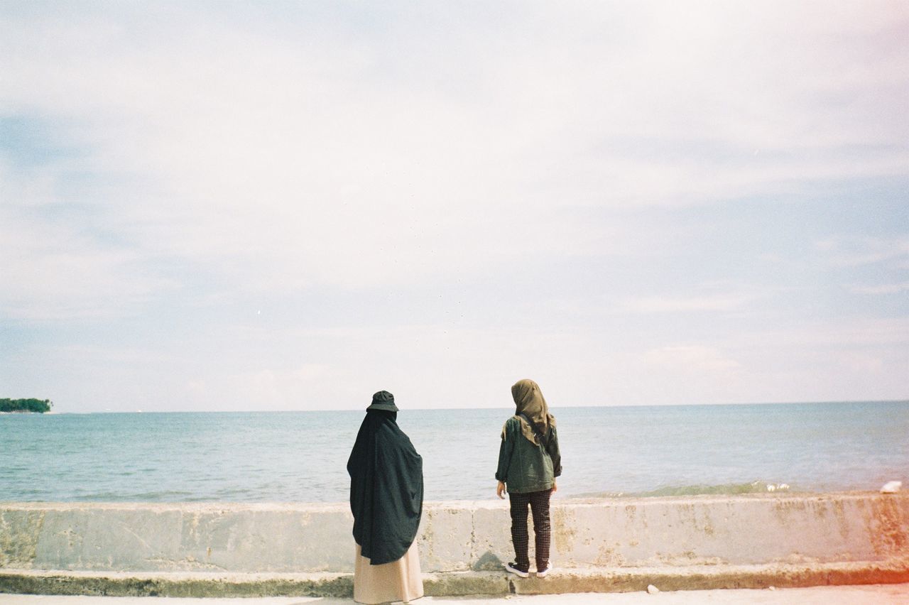 REAR VIEW OF WOMEN AND WOMAN LOOKING AT SEA AGAINST SKY