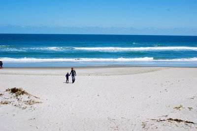 Mid distance view of mother and daughter walking at beach