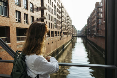 Woman standing by railing in front of buildings at speicherstadt, hamburg, germany