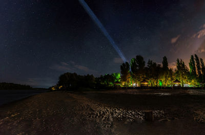 Night view of the forest with illumination, which is located on the shore under the sky with stars