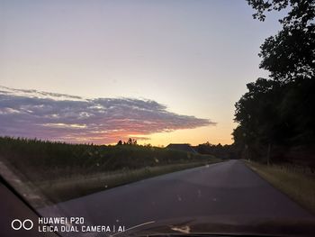 Road by trees against sky during sunset