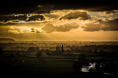 Scenic view of landscape against cloudy sky at sunset