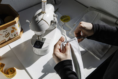 Crop woman sewing details while making handmade fabric mask at home