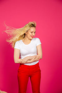 Beautiful young woman standing against pink background
