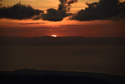 Scenic view of dramatic sky over silhouette landscape during sunset