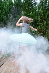 Girl dancing amidst smoke against trees