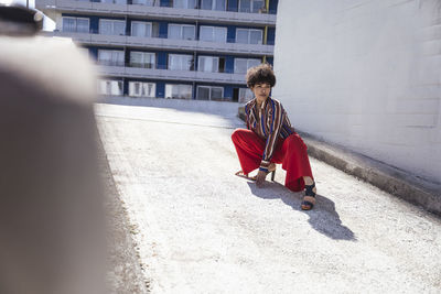 Young woman crouching by wall on sunny day