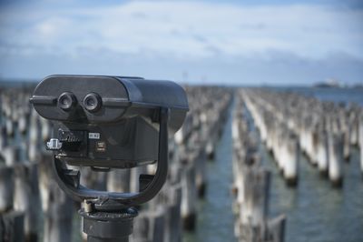 Close-up of coin-operated binoculars by sea against sky