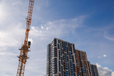 Freshly built high rise apartment building near yellow crane on blue sky background with thin