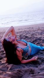 Woman lying down on sand at beach against sky