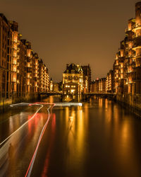 Illuminated buildings by road against sky in city at night