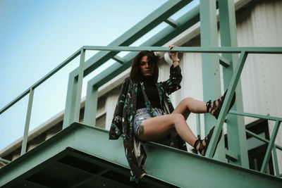 Portrait of woman sitting on staircase against sky