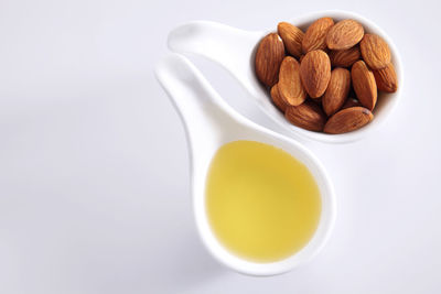 High angle view of almonds and oil in spoon over white background