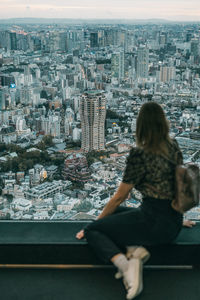 Woman sitting on retaining wall against cityscape