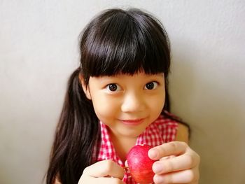 Portrait of cute girl holding apple while sitting against wall