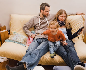 Parents with daughter sitting on sofa at home