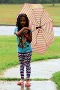 Portrait of girl holding umbrella on footpath at park during rainy season