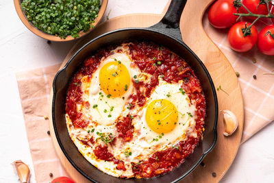 Flat lay image of shakshouka in a pan on a light coloured background close up