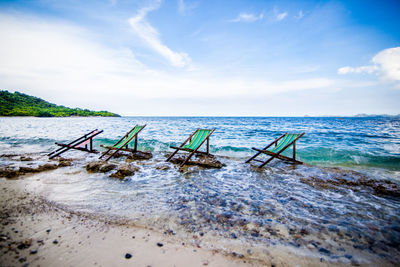 Abandoned deck chairs at beach against sky