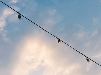 Low angle view of light bulbs hanging against sky