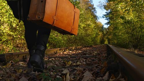 Low section of person walking on railroad track with vintage suitcase