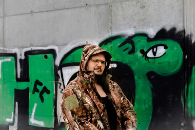 Portrait of smiling young man standing against graffiti wall