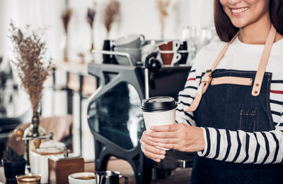 Midsection of smiling barista holding disposable cup in cafe