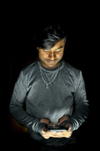 Portrait of young man standing against black background