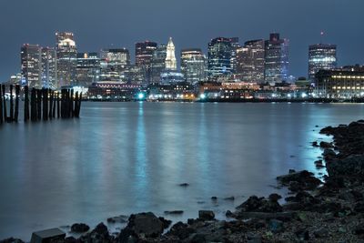 Illuminated cityscape by sea against sky at night