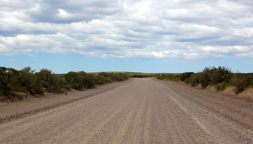 Dirt road amidst landscape against sky