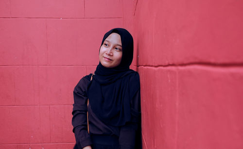 Portrait of beautiful young woman looking away against wall