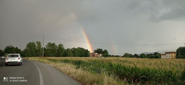 Rainbow over road amidst field against sky