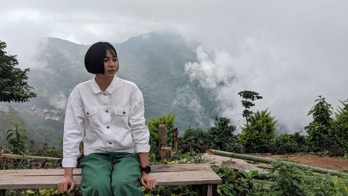 Woman looking away while sitting on seat standing against mountains