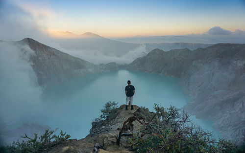 High angle view of man standing on cliff against sky during sunset