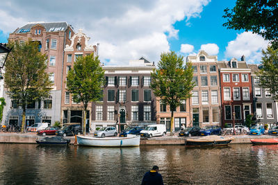 Boats in canal by buildings in city against sky