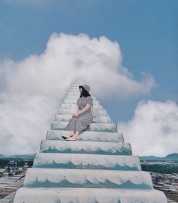 Low angle view of woman sitting on staircase against sky