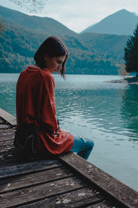 Rear view of girl sitting by lake against mountain