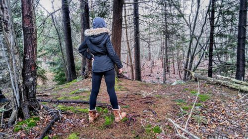 Rear view of woman wearing warm clothing while standing amidst trees in forest