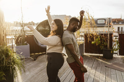 Side view of carefree couple dancing while standing back to back at terrace