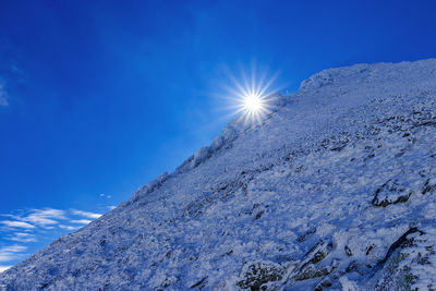 Low angle view of snowcapped mountain against blue sky