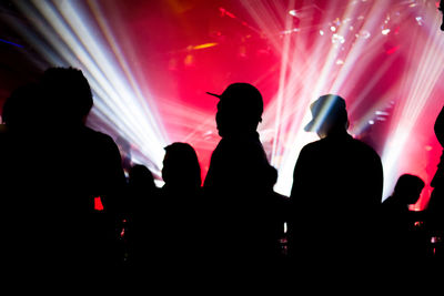 Silhouette people against illuminated light beams at concert