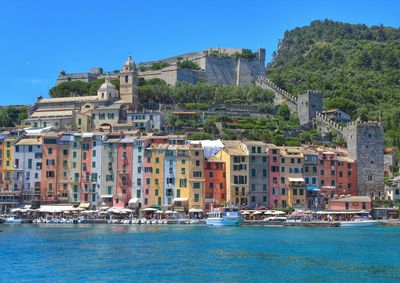 Sailboats in sea by buildings against clear blue sky