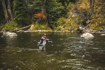 Woman fly fishing at roaring fork river in forest during autumn