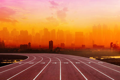 Road by buildings against sky during sunset in city