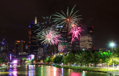 Firework display over river by buildings against sky at night