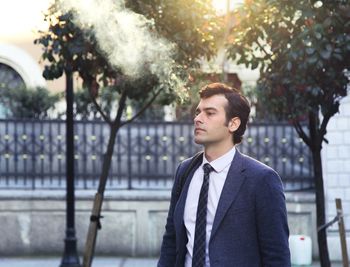 Businessman standing against trees in city