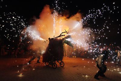 Crowd by firework on footpath at night