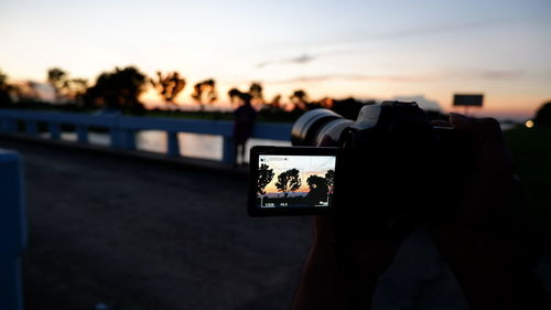 Man photographing with camera phone against sky during sunset